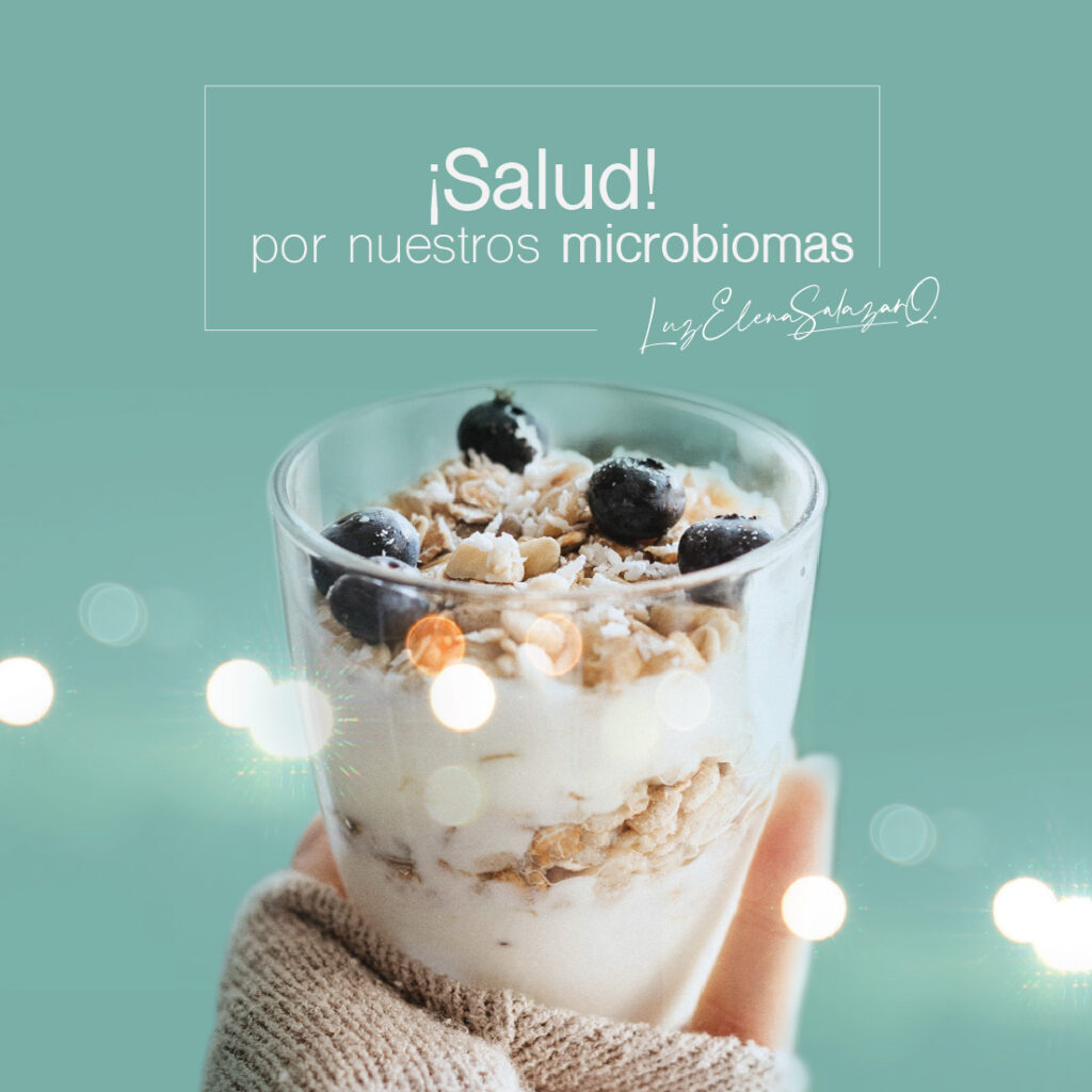 Vaso de yogur natural con granola y arándanos en mano femenina, acompañado del mensaje “¡Salud por nuestros microbiomas!” de la Dra. Luz Elena Salazar, médica funcional en Medellín.